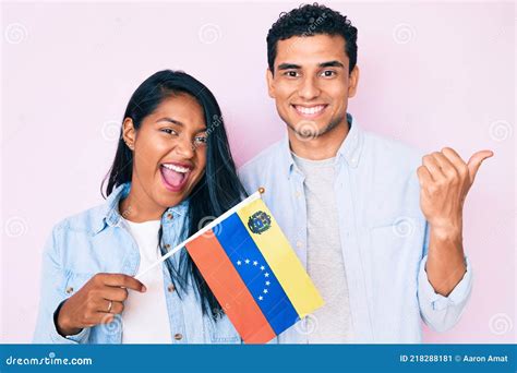Hermosa Pareja Joven Latina Sosteniendo Bandera Venezolana Apuntando El Pulgar Hacia El Lado