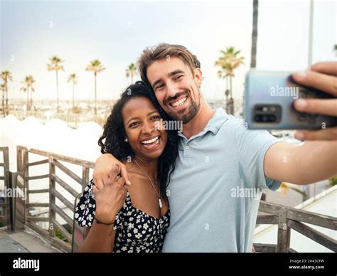 Smiling Multi Ethnic Young Couple Taking A Selfie On A Tropical