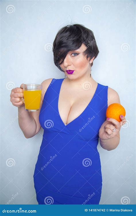 Pretty Chubby Brunette With An Orange Fruit In Her Hand And With Glass Cup With Healthy Juice