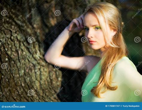 Junge Hübsche Blonde Frau in Der Gelben Kleiderstellung Baumstamm Nähe Und Eis am Sommertag in