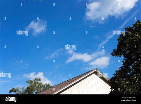 Vivid blue skies with clouds, tree, rooftop and shadows in bright ...