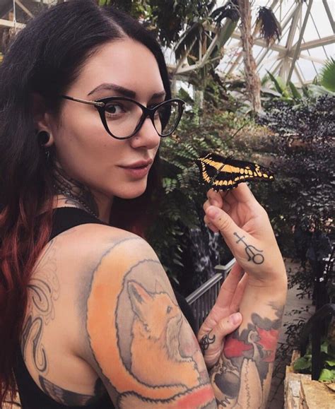 A Woman With Tattoos Holding A Butterfly In Her Right Hand And Looking