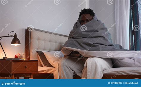 Unwell African American Young Man Shivering Sitting On Bed Wrapped In