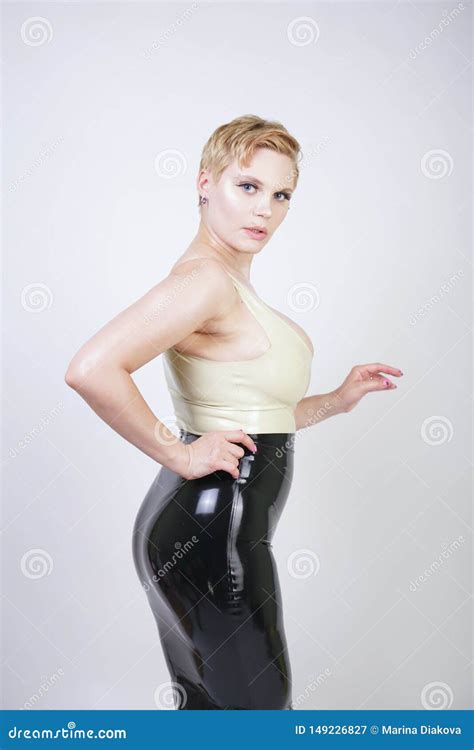 Hot Short Hair Blonde Girl With Curvy Body Wearing Latex Rubber Dress On White Studio Background