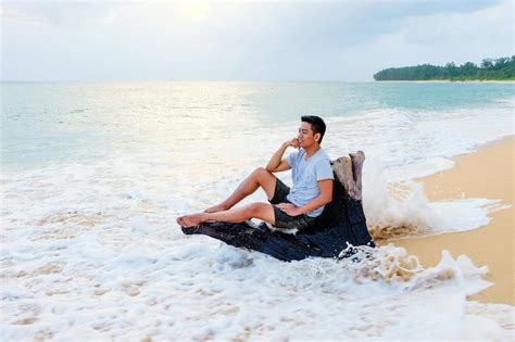 Premium Photo Happy Man Sitting On Driftwood At Beach Against Sky