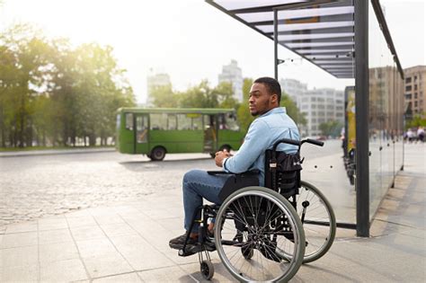 Young Disabled Black Man In Wheelchair Waiting For Public Transport On