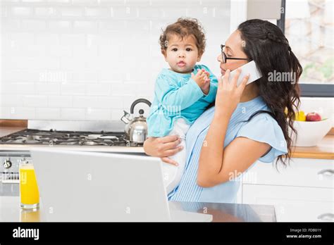Smiling Brunette Holding Her Baby And Using Laptop On Phone Call Stock Photo Alamy