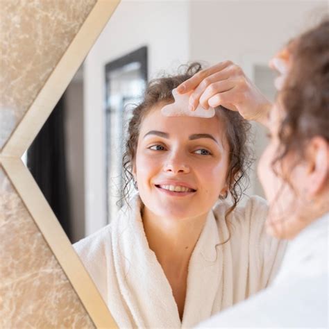 Mulher olhando no espelho e fazendo massagem facial Foto Grátis