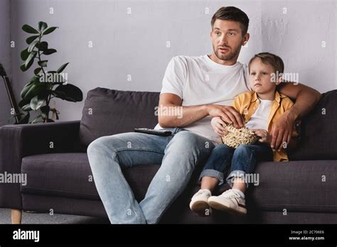 Attentive Father And Son Watching Tv And Eating Popcorn On Sofa At Home