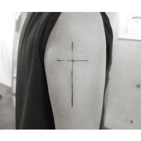 Fine line cross tattoo located on the upper arm.