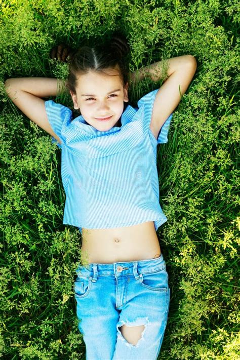 Beautiful Brunette Girl Lies On The Grass With Her Hands Behind Her Head In The Summer And