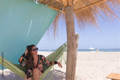 joven mujer latina en traje de baño con túnica floreada y gafas negras disfrutando de la playa