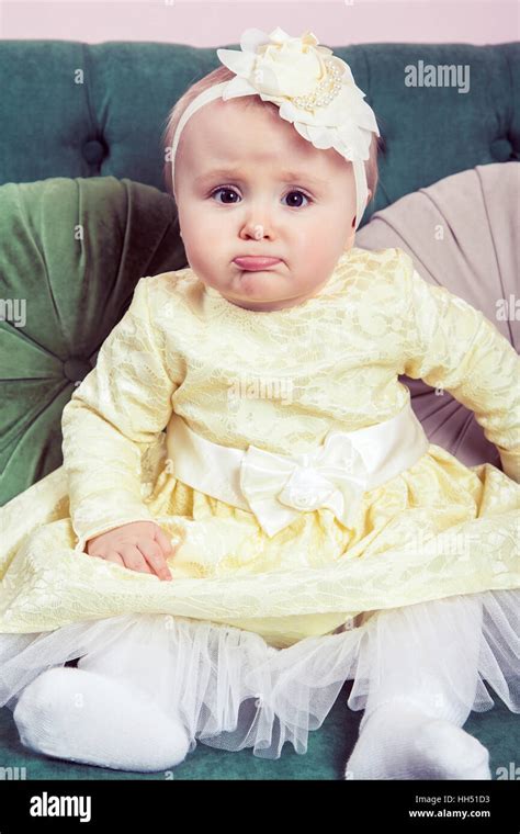 Belle petite fille blonde avec robe jaune et fleur sur sa tête posée sur le canapé vert looking