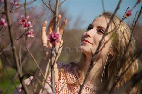 Beautiful Blonde Woman In Pink Dress Walks Through The Flowering Garden In The Spring Stock