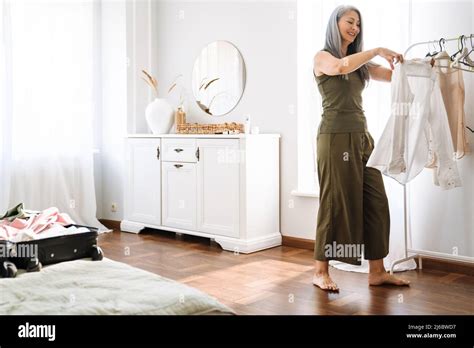 Mature Asian Woman With Grey Hair Smiling While Packing Suitcase At Home Stock Photo Alamy