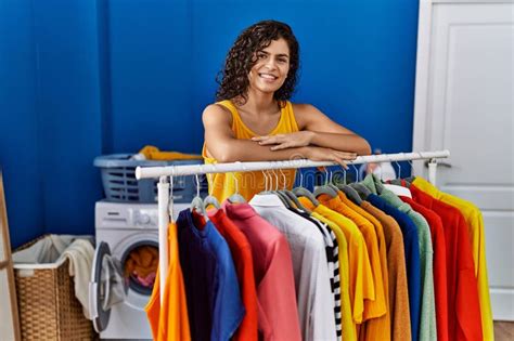 Young Latin Woman Smiling Confident Leaning On Clothes Rack At Laundry