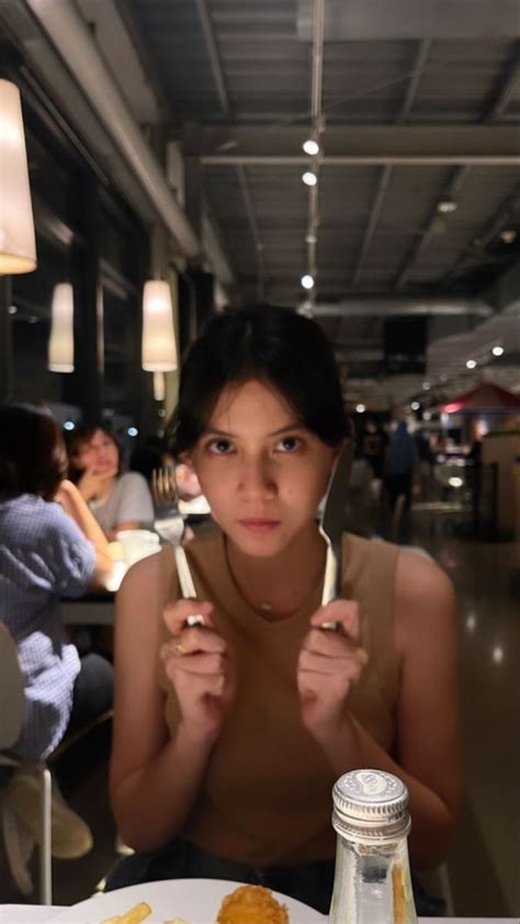 A Woman Sitting At A Table With Food In Front Of Her And Eating From A Fork