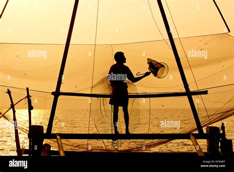 Fisherman Holding A Landing Net In Front Of A Chinese Fishing Net At