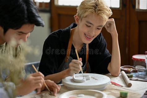 A Happy Asian Gay Man Enjoys Painting A Ceramic Plate In A Workshop With His Boyfriend Stock