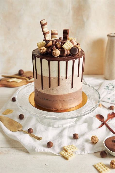Vertical Shot Of Chocolate Ombre Naked Cake With Sweets And Chocolate Drip On Glass Cake Stand