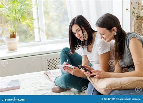 Two Brunette Girls Are Sitting Talking Holding A Book And A Phone Stock Image Image Of