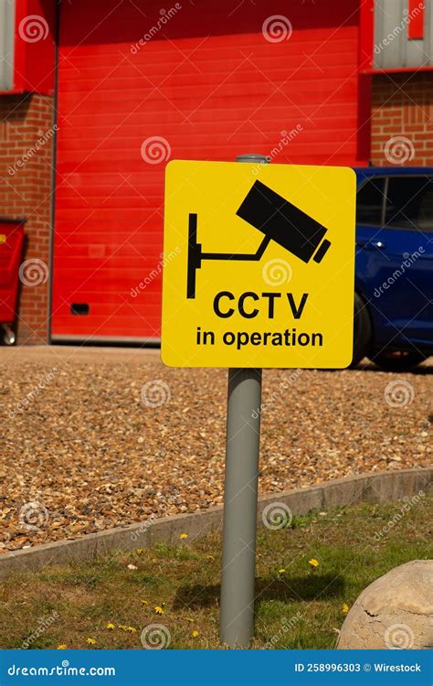 Vertical Shot Of A Yellow Warning Sign With Cctv In Operation Against