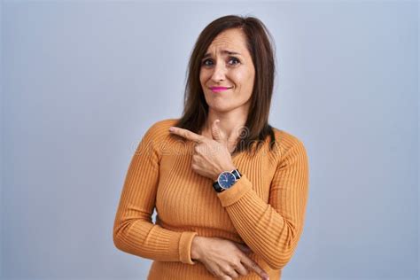 Middle Age Brunette Woman Standing Wearing Orange Sweater Pointing Aside Worried And Nervous