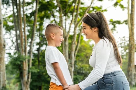 Joven madre latina de rodillas mirando con orgullo a su hijo pequeño mientras juega en un parque