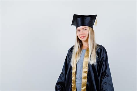 Fille blonde debout tout droit et se présentant à la caméra en robe de graduation et casquette