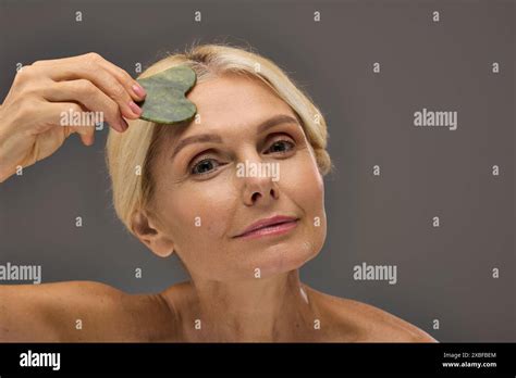 Charming Mature Woman Using Gua Sha On A Gray Backdrop Stock Photo Alamy