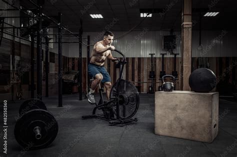 Foto De Powerful Muscular Male Athlete With A Naked Torso Trains With An Air Bike In A Modern