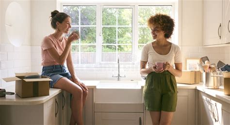 Two Female Friends Or Same Sex Couple Taking A Coffee Break From Unpacking On Moving Day In New