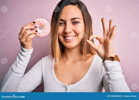 Jeune Belle Femme Blonde Aux Yeux Bleus Tenant Doughnut Rose Sur Fond Faire Ok Signe Avec Les