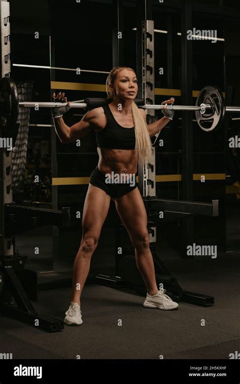 A Sporty Woman With Blonde Hair Is Squatting With A Barbell Near The Squat Rack In A Gym A Girl
