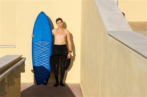 Premium Photo A Man With Naked Torso Standing By The Wall Holding A Surfboard