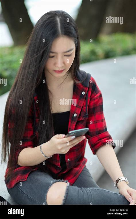 Female Teenager Sitting In City Street Messaging To Her Friends Using Smartphone For Wasting