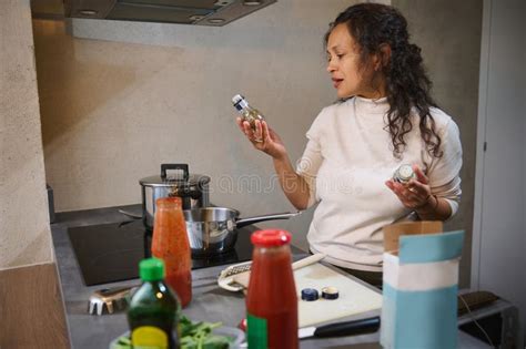 Beautiful Curly Hired Brunette Woman Housewife Holding Small Bottle With Culinary Herbs