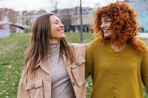 Premium Photo Joyful Redhead And Brunette Women Laughing Together In A Park Setting