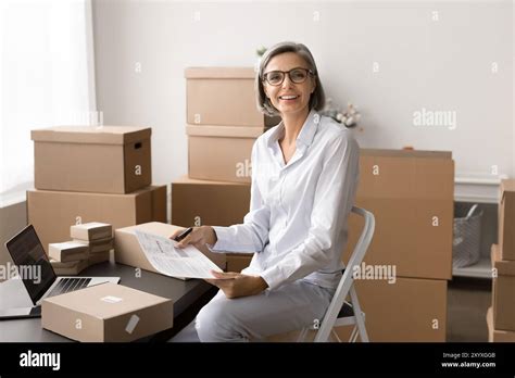 Mature Woman Sits In Workspace Surrounded By Boxes And Packages Stock