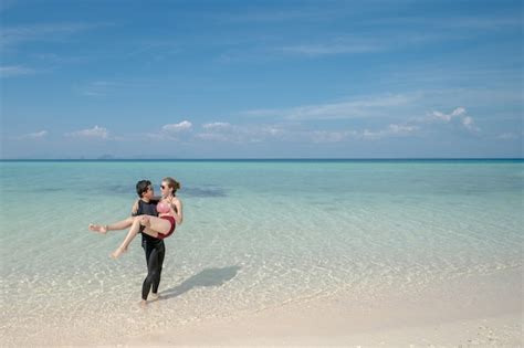 Hombre Que Lleva A La Mujer Del Bikini En El Agua De Mar Por La Playa De Arena Blanca Paisaje