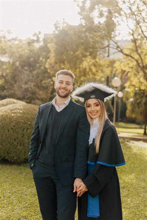 A Man And Woman In Graduation Gowns Pose For A Photo Together On The Grass