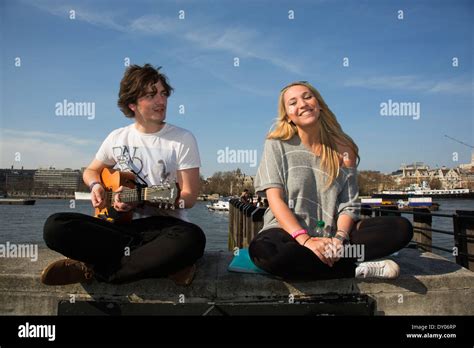 Two young buskers singing and playing guitar on the riverside wall ...