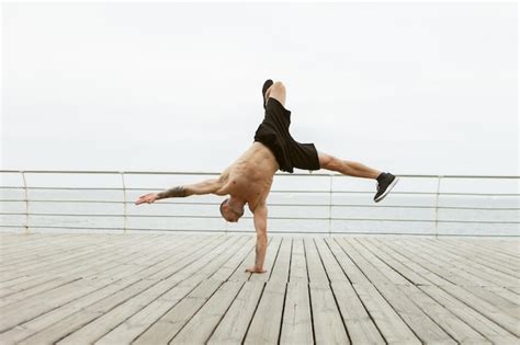 Premium Photo Muscular Bodybuilder Fitness Man With A Naked Torso Stands On One Arm On The Beach