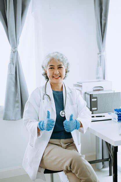 Premium Photo Confident Mature Asian Female Doctor In White Medical Uniform Sit At Desk