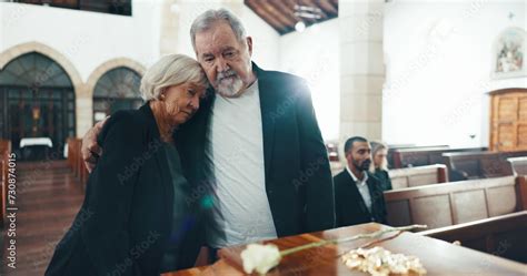 Funeral, coffin and senior couple hug in church for goodbye, mourning and grief in memorial ...