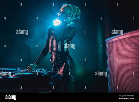 Happy Dj Woman With Blonde Hair Listening Music And Touching Headphones In Nightclub With Smoke