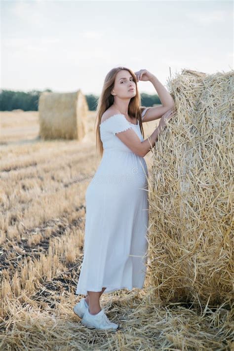 Beautiful Pregnant Brunette In A White Dress Near The Haystacks In The Field At Sunset Stock
