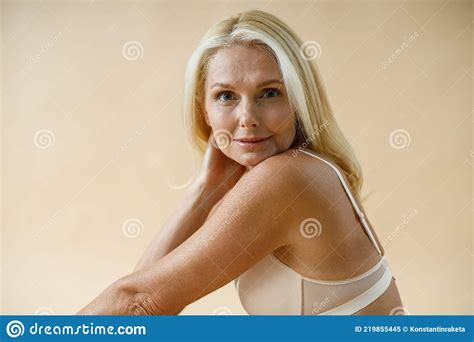 Portrait Of Sensual Mature Blonde Woman Posing In Underwear Sitting On Floor And Looking At