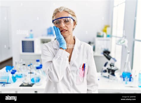 Femme blonde d âge moyen travaillant au laboratoire scientifique touchant la bouche avec la main
