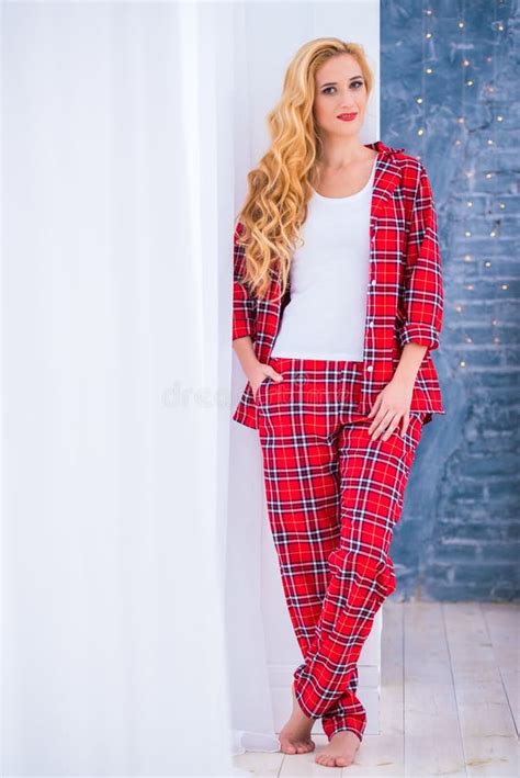 Beautiful Blonde Woman In Red Checkered Pajamas Sits Near The Window And Demonstrates